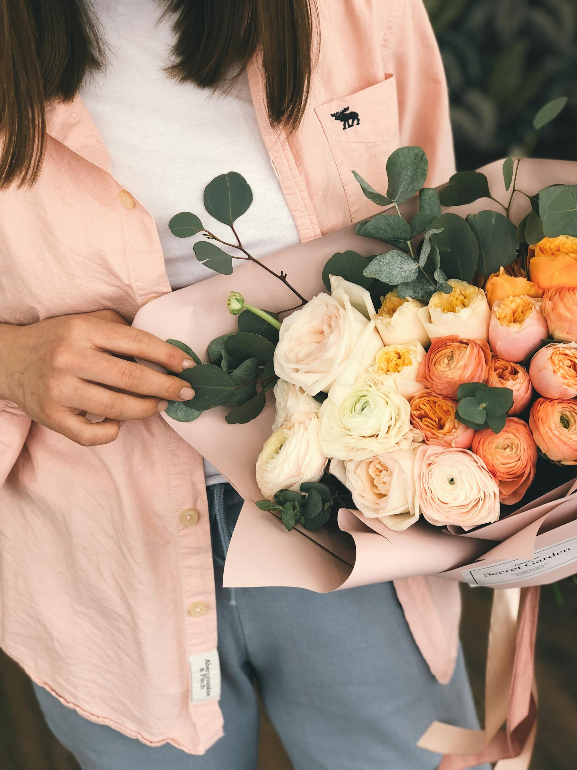 Close-up of a woman holding a colorful bouquet of roses and eucalyptus leaves, adding a touch of natural beauty.