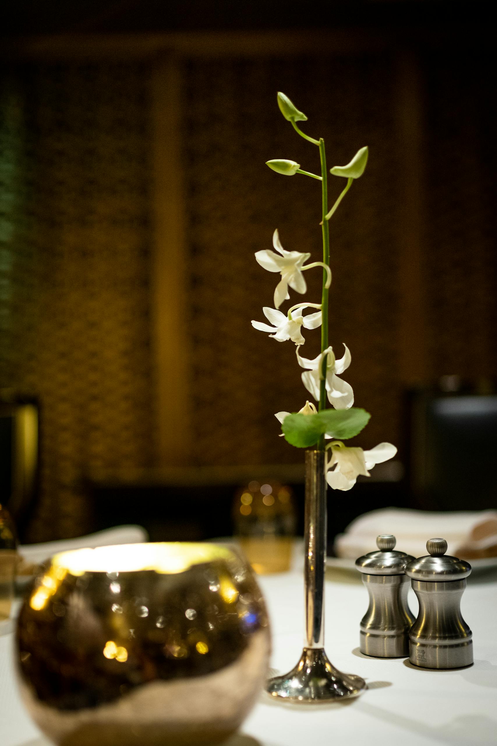A sophisticated dining table setup featuring a single orchid in a sleek vase and ambient decor.