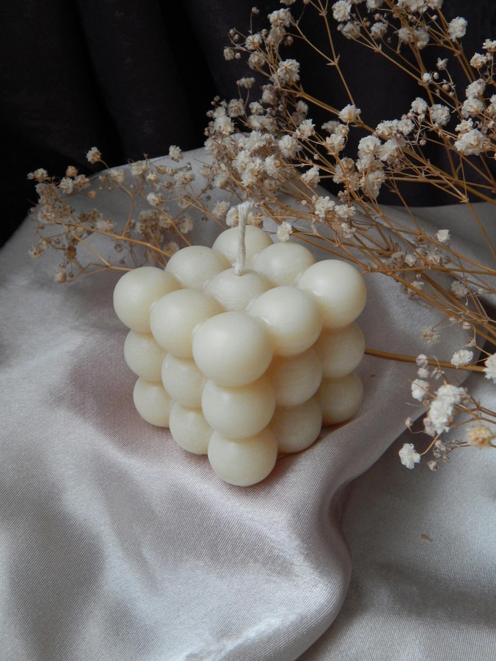 A unique bubble-shaped candle surrounded by dried flowers on a silky fabric backdrop.
